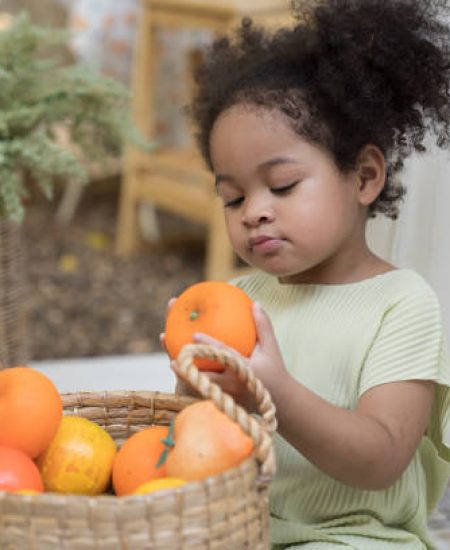 African American little girl playing alone with fruits in basket in the garden